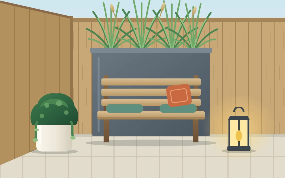 A corner bench on a patio with a tall narrow planter of grasses behind it and a lantern standing on the paving beside it